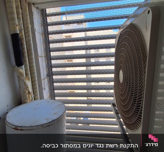 יחידת מזגן ומיכל מים ליד חלון עם רשת